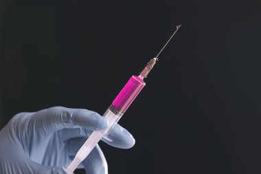 Doktorlar mavi eldivenli ellerinde siyah arka planda izole edilmiş kırmızı sıvıyla bir şırınga tutuyorlar..