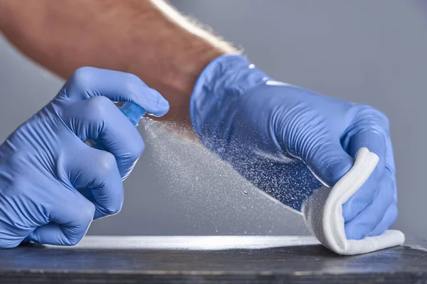 Les mains en gants de caoutchouc traitent la table avec un désinfectant pulvérisé sur un fond gris. Désinfection des locaux — Photo