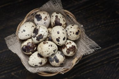 Tahta bir masada hasır sepetin içinde taze bıldırcın yumurtalarının yatay görüntüsü..