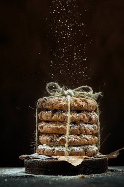 İple bağlanmış yuvarlak kurabiyelerin dikey görüntüsü kahverengi arkaplanda pudra şekeri serpiştirilir..