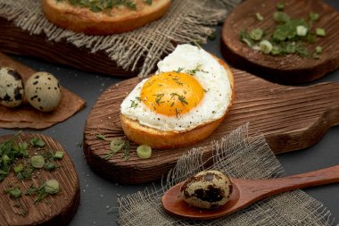 Çöreğin üstünde kahvaltılık yumurta, bıldırcın yumurtası, ahşap tabakta yeşillikler..