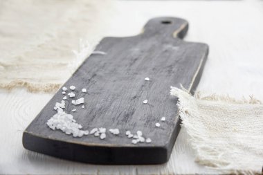 Beyaz ahşap bir masada tahta kesme tahtasının yatay görüntüsü. Tahtaya dağılmış deniz tuzu.