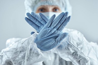 Tıbbi maskeli, lastik eldivenli ve takım elbiseli bir doktor dur işareti yapıyor. Koronavirüsle yüzleşmek.