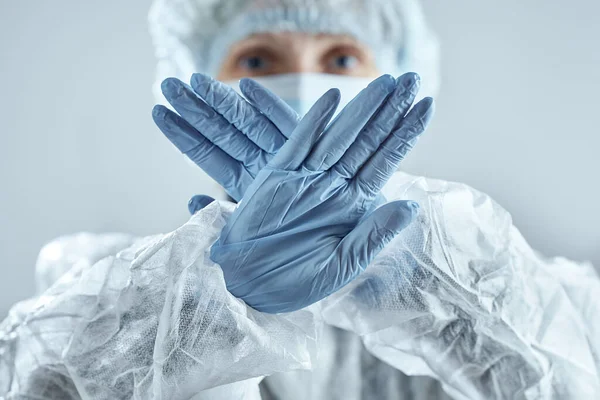 Tıbbi maskeli, lastik eldivenli ve takım elbiseli bir doktor dur işareti yapıyor. Koronavirüsle yüzleşmek.
