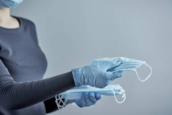 Horizontal shot of girl in disposable gloves gives medical masks on a gray background. Photo with copy space.