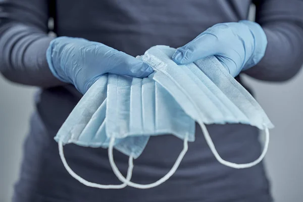 Horizontal shot of hands in blue disposable gloves holding medical masks holding medical masks. Front view.