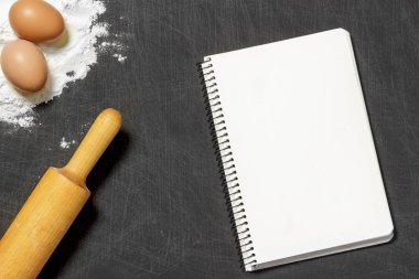Hamur için malzemeler. Un, yumurta, oklava ve siyah scratchet arka plan üzerinde boş not defteri. Üstten Görünüm. Düz yatıyordu. Mockup menü veya tarifi.