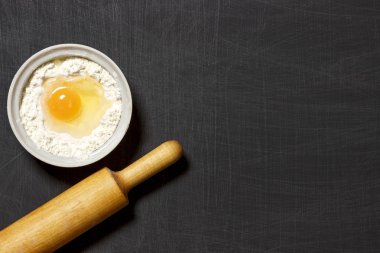 Hamur için malzemeler. Un, yumurta ve merdane siyah scratchet arka plan üzerinde. Üstten Görünüm. Düz yatıyordu.