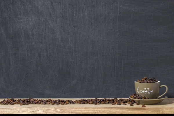 Cup and brown roasted coffee beans scattered on the background of a blank scratched blackboard. Mock up — Stock Photo, Image