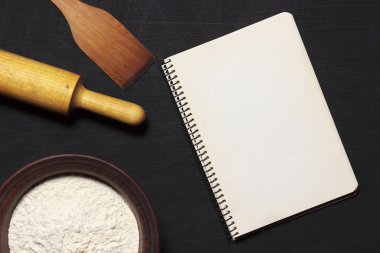 Hamur için malzemeler. Un, arka plan üzerinde siyah bir haddeleme pin ve boş not defteri kaşıdı. Üstten Görünüm. Düz yatıyordu. Mockup menü veya tarifi.