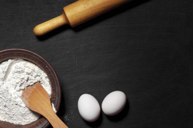 Hamur için malzemeler. Un, yumurta, oklava ve siyah bir çizik arka plan boş tahta. Üstten Görünüm. Düz yatıyordu. Mockup menü veya tarifi.