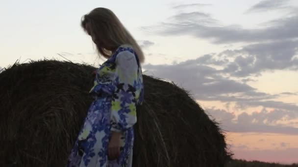 Ξανθιά κοπέλα σε ένα μακρύ φόρεμα κοντά τα δεμάτια άχυρου — Αρχείο Βίντεο