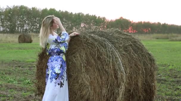 Blond meisje in een lange jurk in de buurt van de bundels stro — Stockvideo