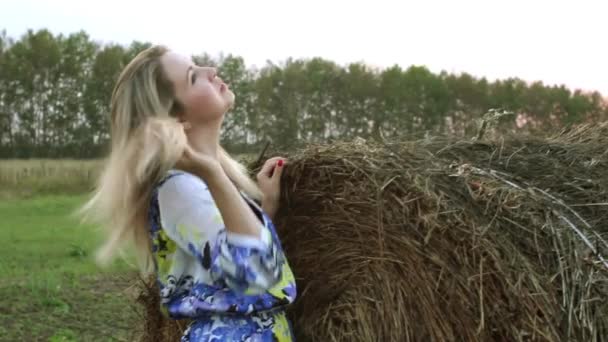 Blond meisje in een lange jurk in de buurt van de bundels stro — Stockvideo