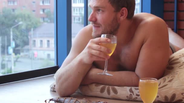 Man drinken bier uit een glas en eet vis, liggend op de vloer — Stockvideo