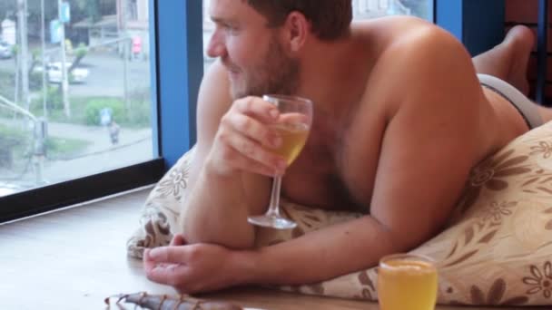 Homme buvant de la bière dans un verre et mangeant du poisson, couché sur le sol — Video