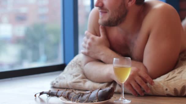 Man drinking beer from a glass and eat fish, lying on the floor — Αρχείο Βίντεο