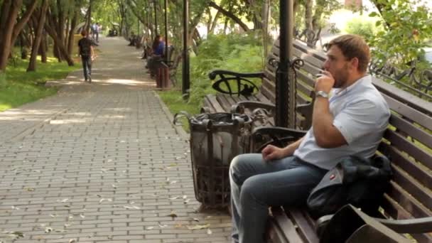 Man smokes on the bench in the park — Stock Video