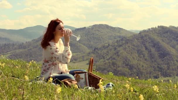 Mulher bebendo vinho sentado em um prado verde no alto das montanhas — Vídeo de Stock