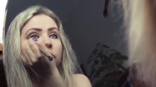 Красивая блондинка делает вечерний макияж у зеркала — стоковое видео