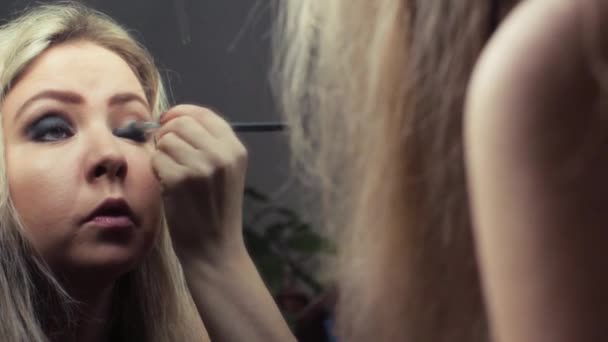Hermosa chica rubia haciendo maquillaje de noche cerca del espejo — Vídeos de Stock