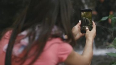 genç kadın bir şelale bir smartphone cep telefonu ile seyahat ederken alır