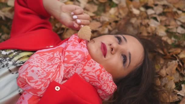 Портрет девушки, которая лежит на осенней листве в парке — стоковое видео