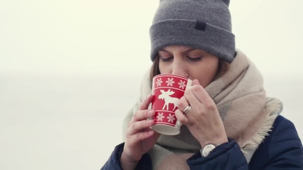 Mujer joven disfrutando de su café o té de la mañana en el fondo de un horizonte nevado mientras camina — Vídeos de Stock