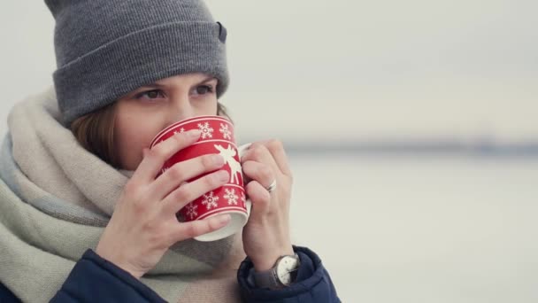 Young woman enjoying her morning coffee or tea on the background of a snowy horizon while walking — Stock Video