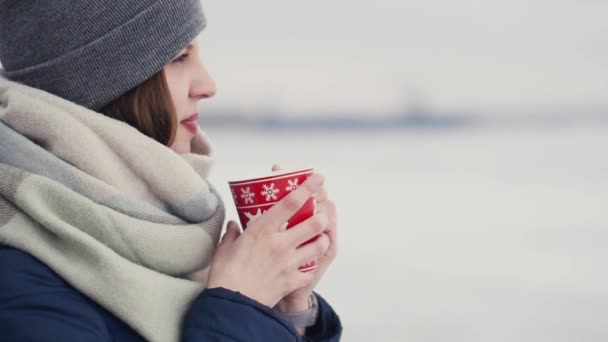 Νεαρή γυναίκα απολαμβάνοντας τον πρωινό καφέ ή τσάι στο φόντο του ορίζοντα σε μια χιονισμένη ενώ το περπάτημα — Αρχείο Βίντεο