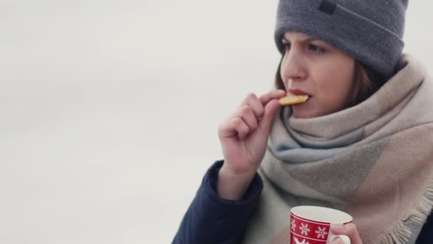 Jonge vrouw haar's ochtends koffie of thee op de achtergrond van een besneeuwde horizon genieten tijdens het lopen — Stockvideo