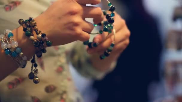 Een jonge vrouw probeert op armbanden op de markt — Stockvideo