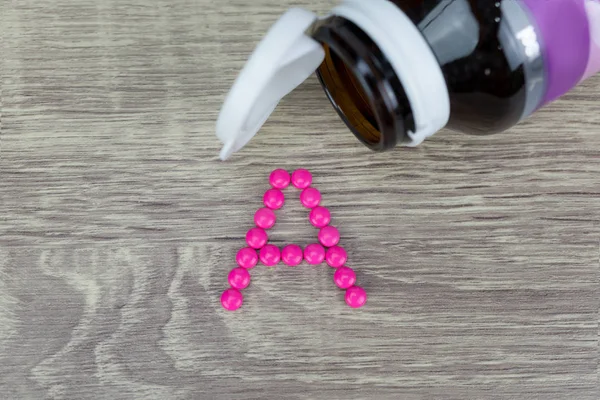 Pil merah muda bentuk ke A alfabet di latar belakang kayu — Stok Foto