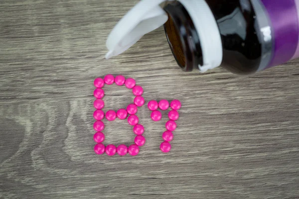 Píldoras rosadas que forman la forma del alfabeto B7 sobre fondo de madera — Foto de Stock