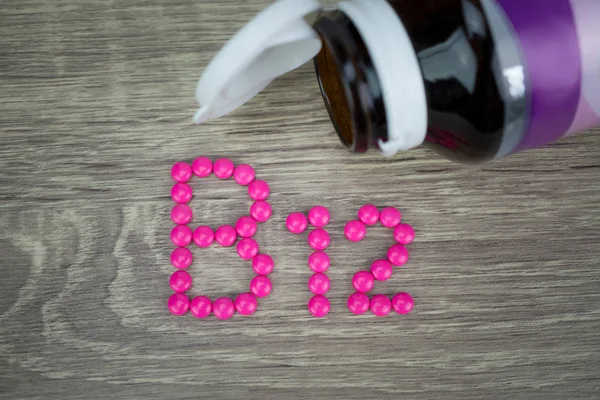 Rosa Pillen formen Form zu B12-Alphabet auf Holz-Hintergrund — Stockfoto