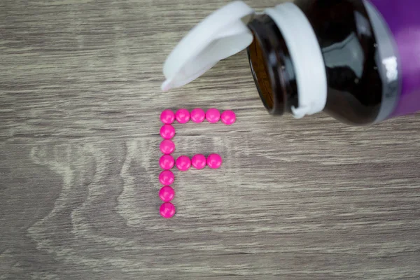 Pílulas cor-de-rosa formando forma para o alfabeto F no fundo de madeira — Fotografia de Stock