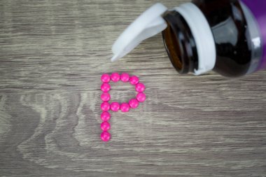 Pink pills forming shape to P alphabet on wood background clipart