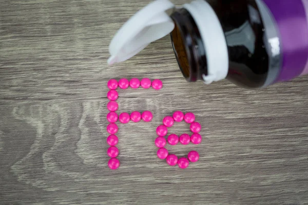 Pílulas cor-de-rosa formando forma para alfabeto Fe no fundo de madeira — Fotografia de Stock