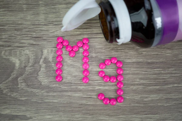 Pílulas cor de rosa formando forma para o alfabeto Mg no fundo de madeira — Fotografia de Stock
