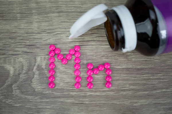 Pílulas cor de rosa formando forma para o alfabeto Mn no fundo de madeira — Fotografia de Stock