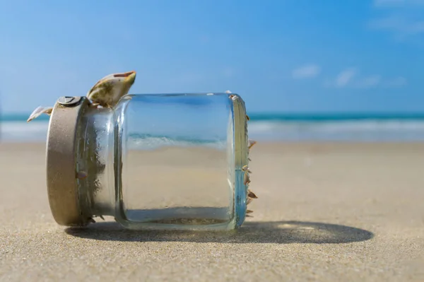 Lege glazen fles aan zandstrand met blauwe hemel en zee — Stockfoto