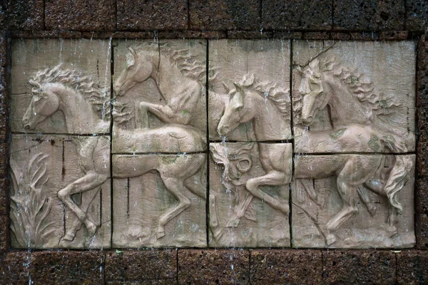 Escultura de pedra de cavalos na parede com cachoeira — Fotografia de Stock