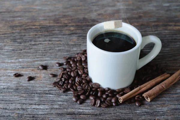 Cubo de azúcar moreno cayendo en taza de café caliente con granos de café — Foto de Stock