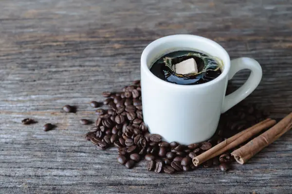 Cubo de azúcar moreno cayendo en taza de café caliente con granos de café — Foto de Stock
