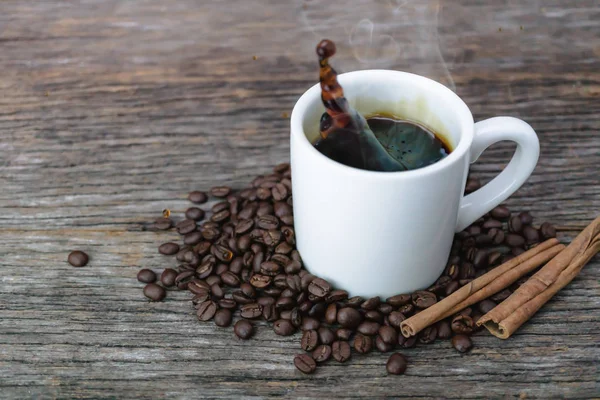 Café chaud en tasse blanche avec éclaboussures et grains de café sur bac à bois — Photo