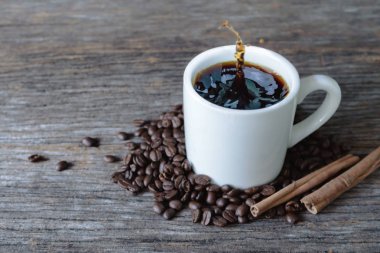 Sıçrama ve ahşap bac üzerinde kahve çekirdekleri ile beyaz kupa sıcak kahve