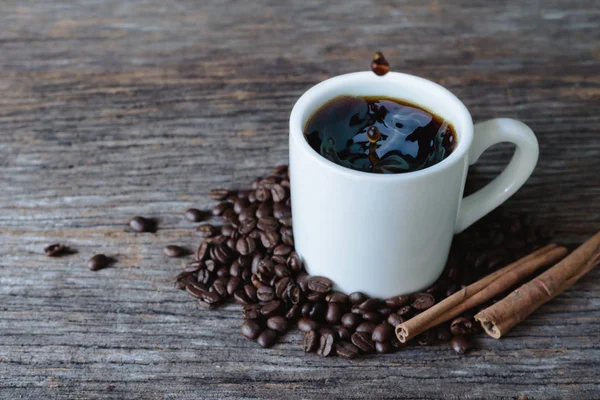 Café caliente en taza blanca con salpicaduras y granos de café en bac de madera — Foto de Stock