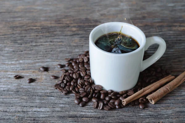 Café caliente en taza blanca con salpicaduras y granos de café en bac de madera — Foto de Stock