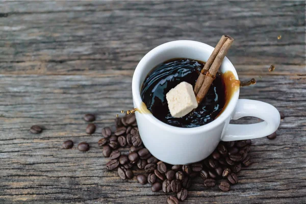 Cubo de azúcar moreno cayendo en taza de café caliente con granos de café — Foto de Stock