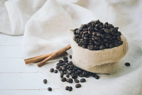 Granos de café en saco de arpillera y canela sobre fondo de madera — Foto de Stock